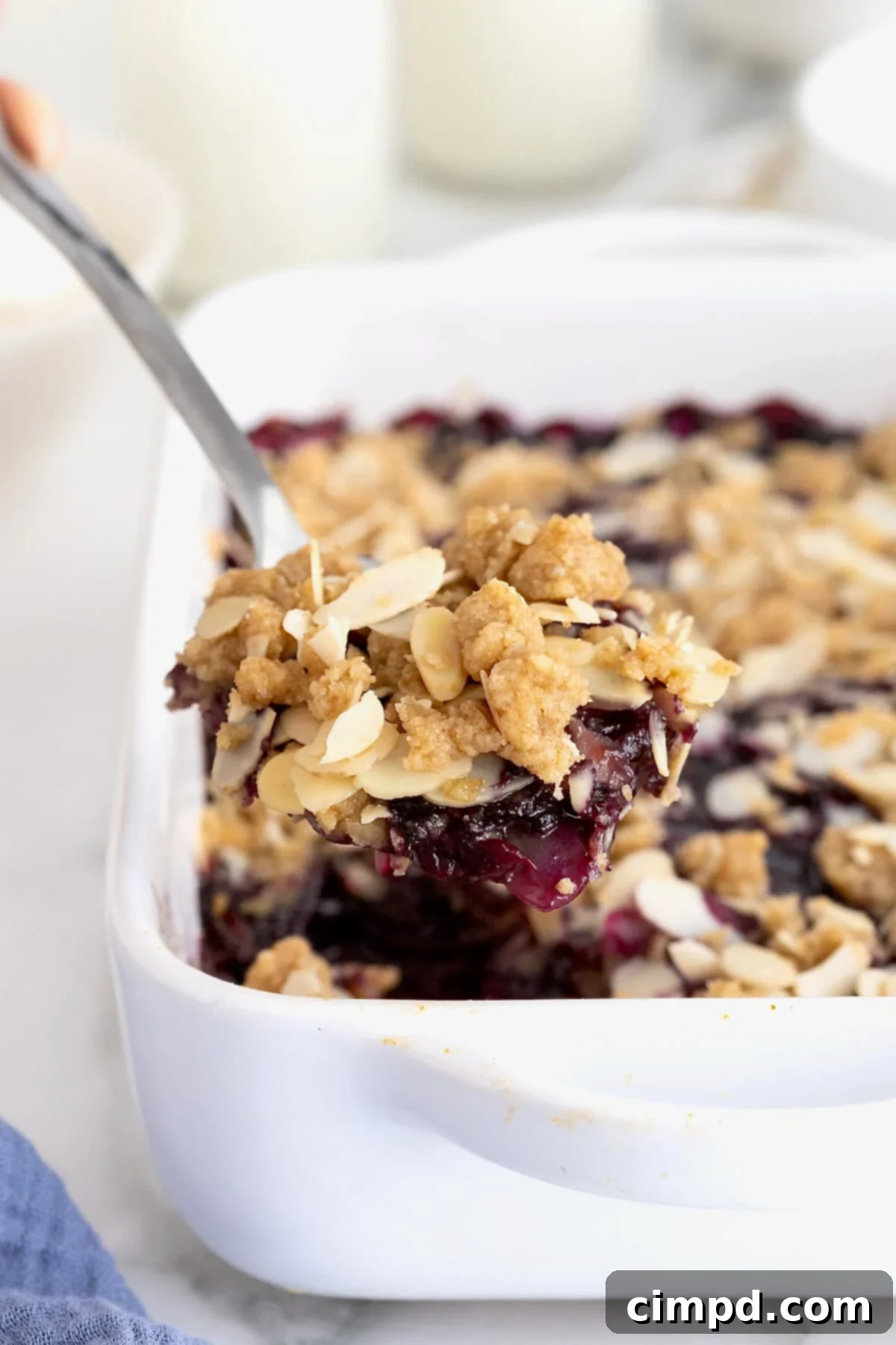 A spoonful of blueberry almond crips being lifted from a small white casserole dish of blueberry crisp