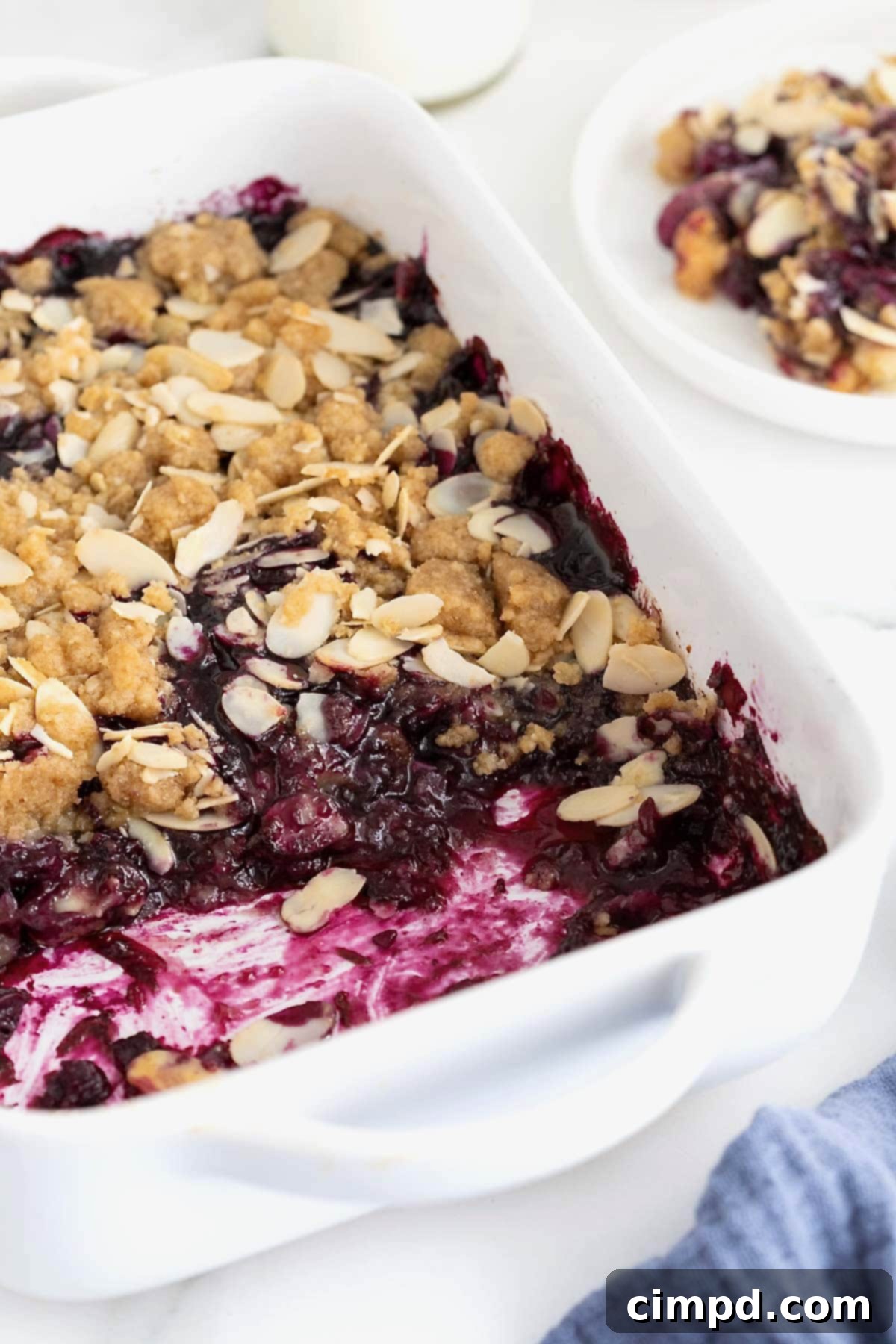 A white baking dish of blueberry almond crisp on a white marble counter.