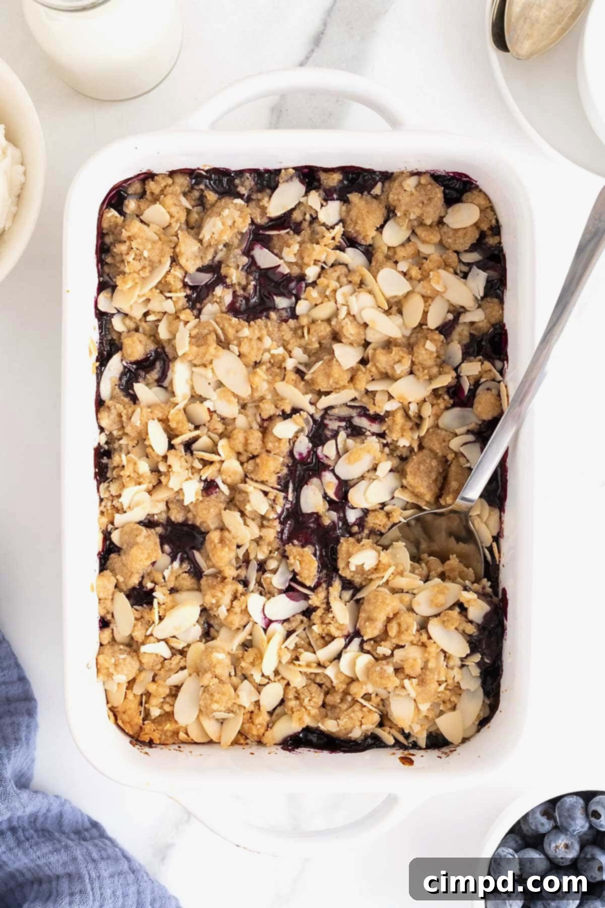 A white baking dish of blueberry almond crisp on a white marble counter.