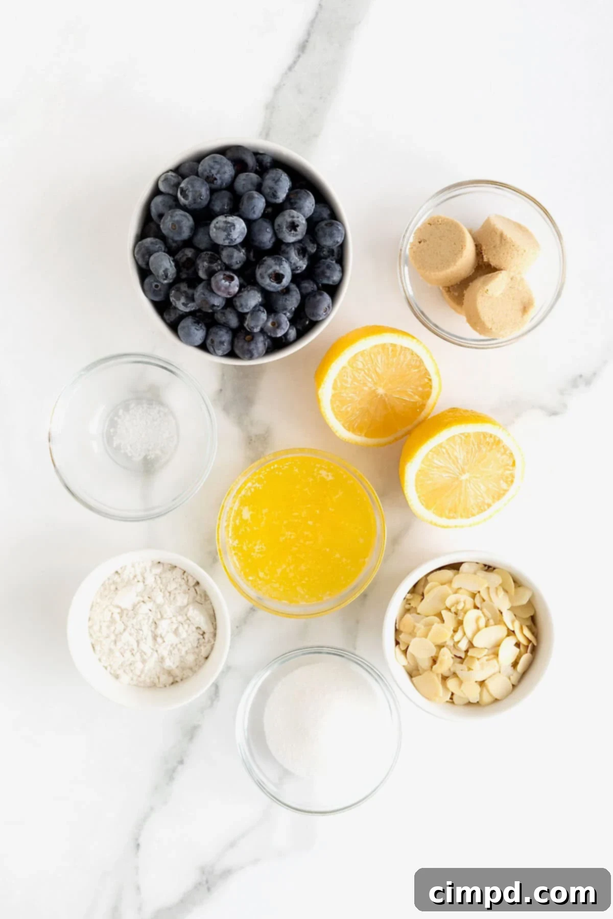 Ingredients to make blueberry almond crisp in small glass dishes on a white marble counter.