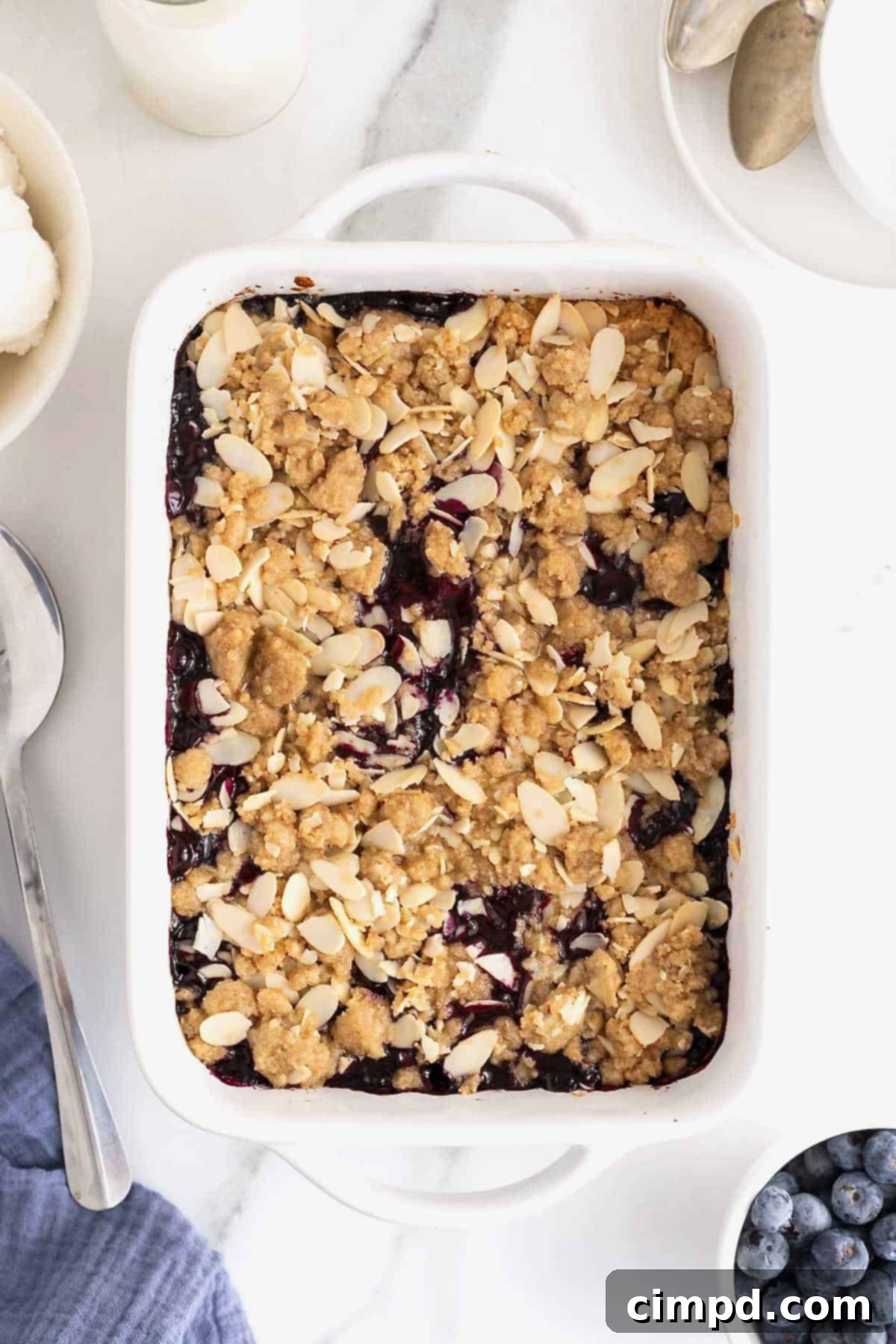 A white baking dish of blueberry almond crisp on a white marble counter.