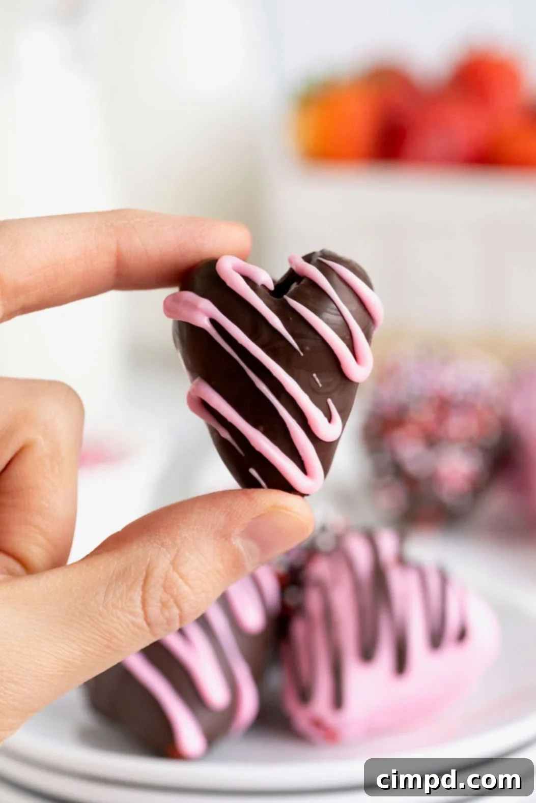 Sweetheart Chocolate Strawberries 3 A perfectly formed heart-shaped chocolate covered strawberry, delicately held between a thumb and forefinger, showcasing its intricate details and tempting appeal.