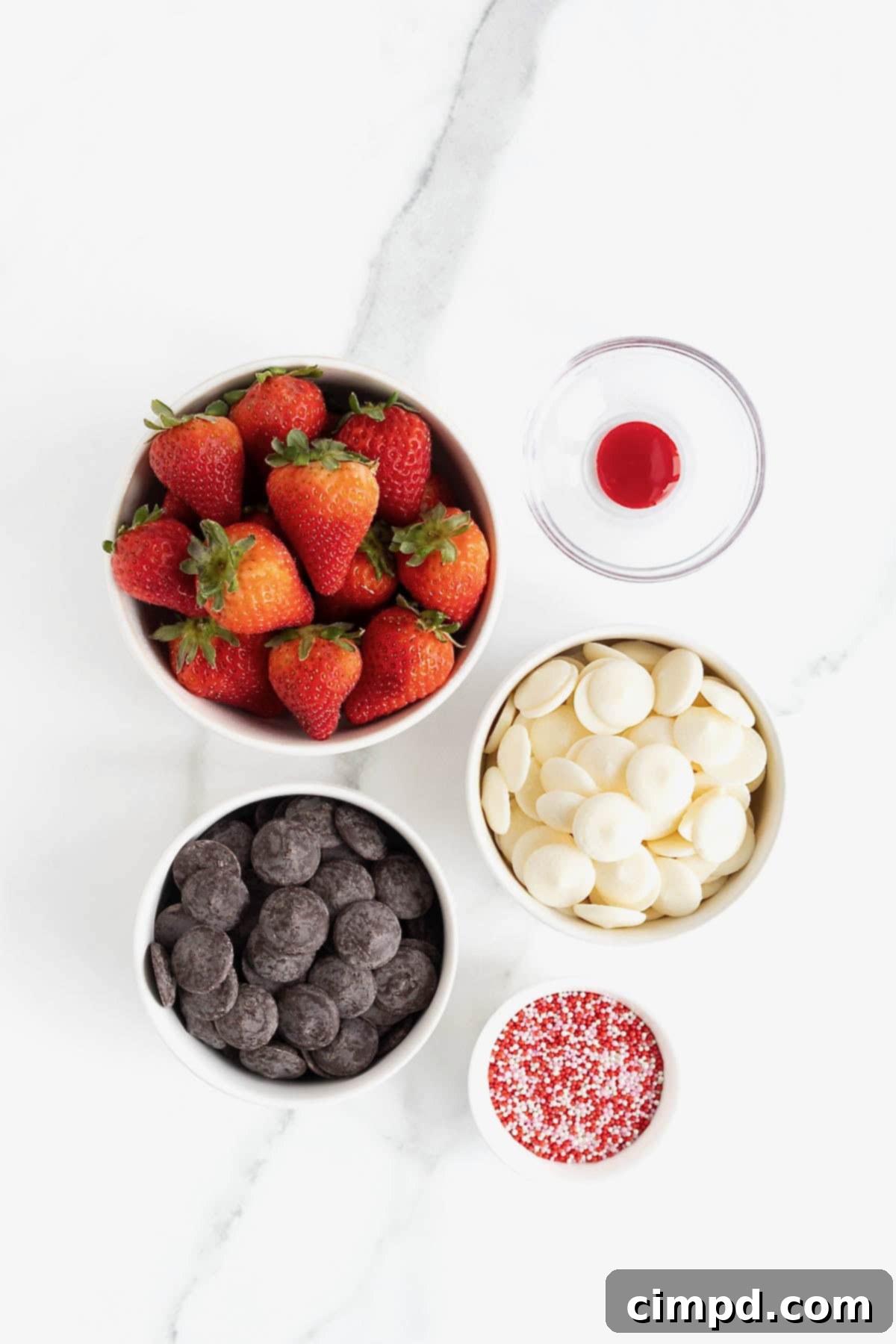 Sweetheart Chocolate Strawberries 6 An array of ingredients for heart-shaped chocolate covered strawberries, neatly arranged in small glass dishes on a pristine white marble counter, ready for preparation.