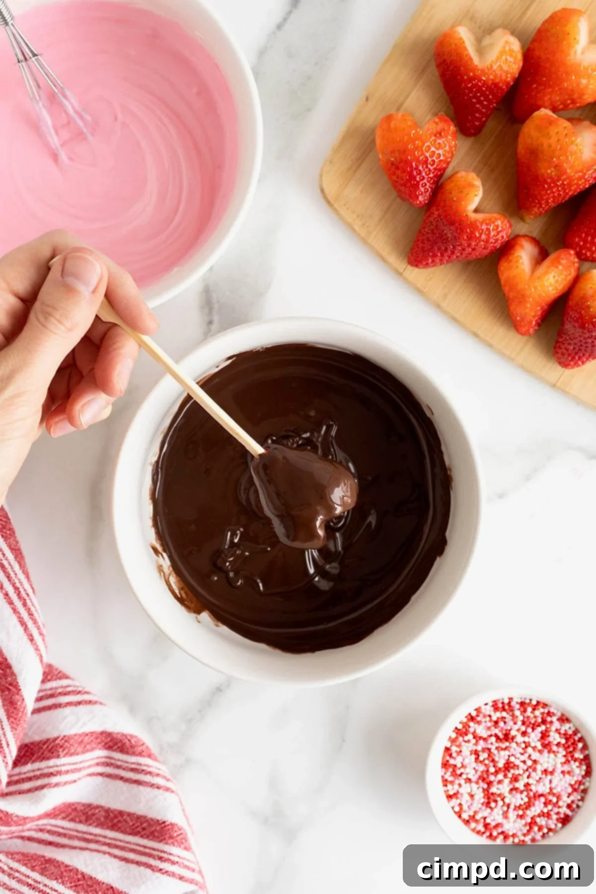 Sweetheart Chocolate Strawberries 9 A heart-shaped strawberry in the process of being dipped into rich, melted chocolate, creating a luscious coating.