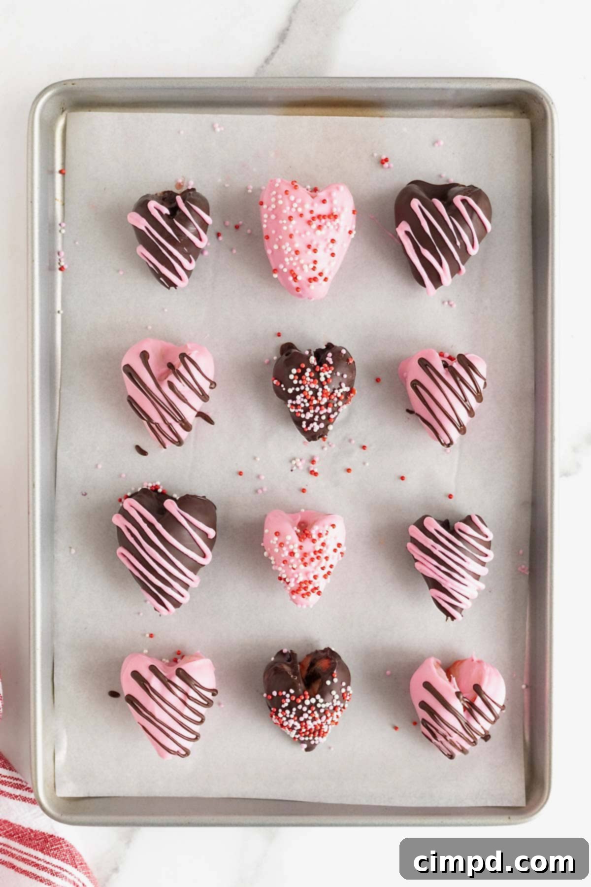 Sweetheart Chocolate Strawberries 10 A collection of chocolate-covered heart-shaped strawberries, meticulously arranged on a parchment-lined aluminum baking sheet, awaiting their final set.