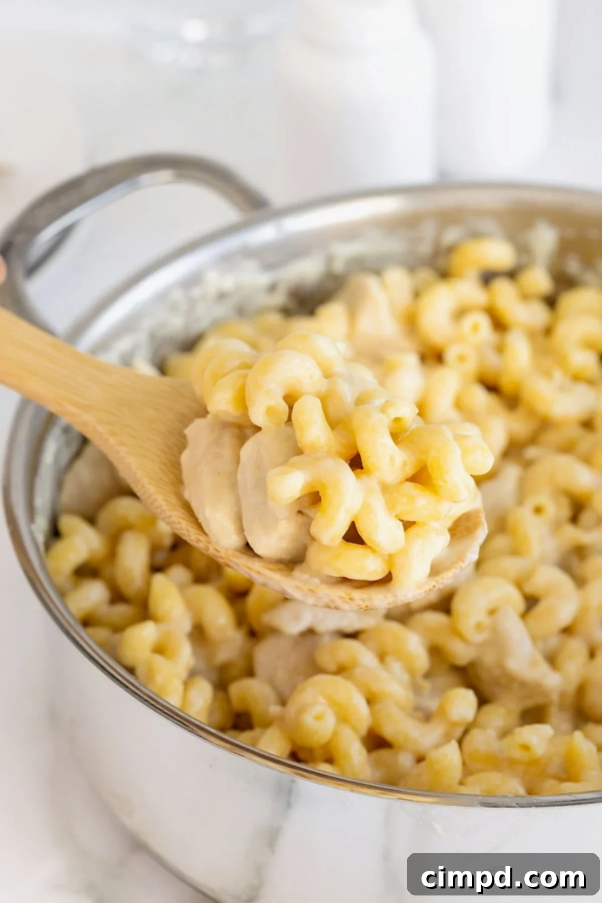 A wooden spoon scooping chicken Alfredo pasta from a stainless steel pot.