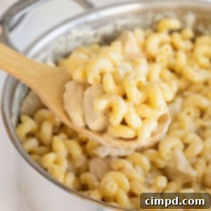 A wooden spoon scooping chicken Alfredo pasta from a stainless steel pot.