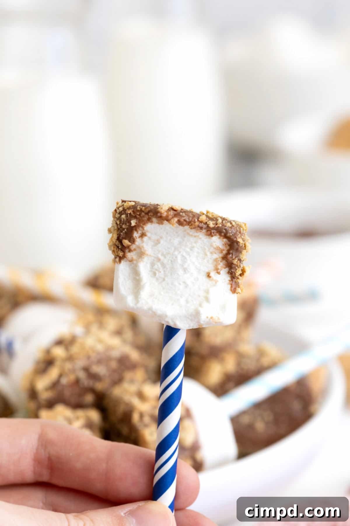 A marshmallow pop on a blue and white striped stick. The marshmallow has a bite out of it.