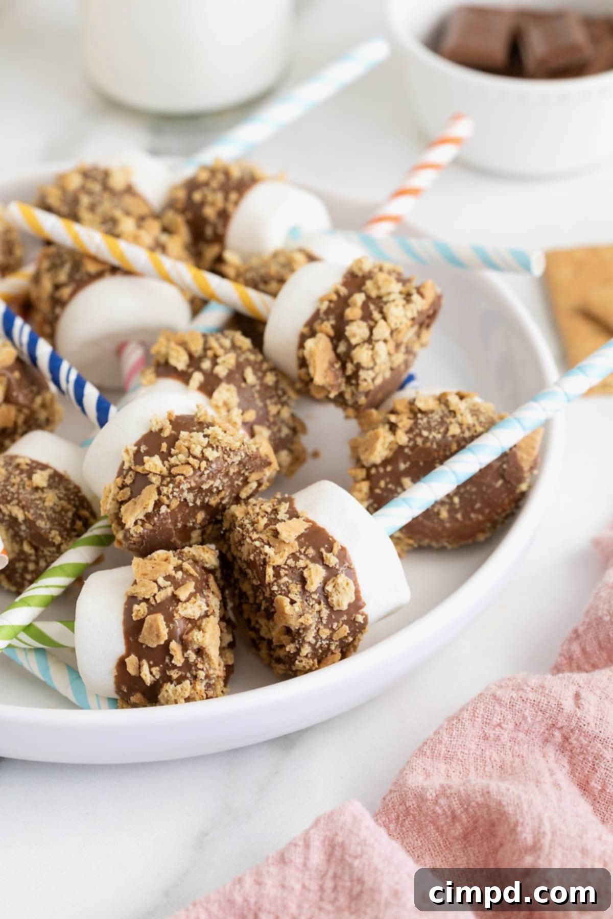 A pile of marshmallow pops on a white rimmed serving plate.
