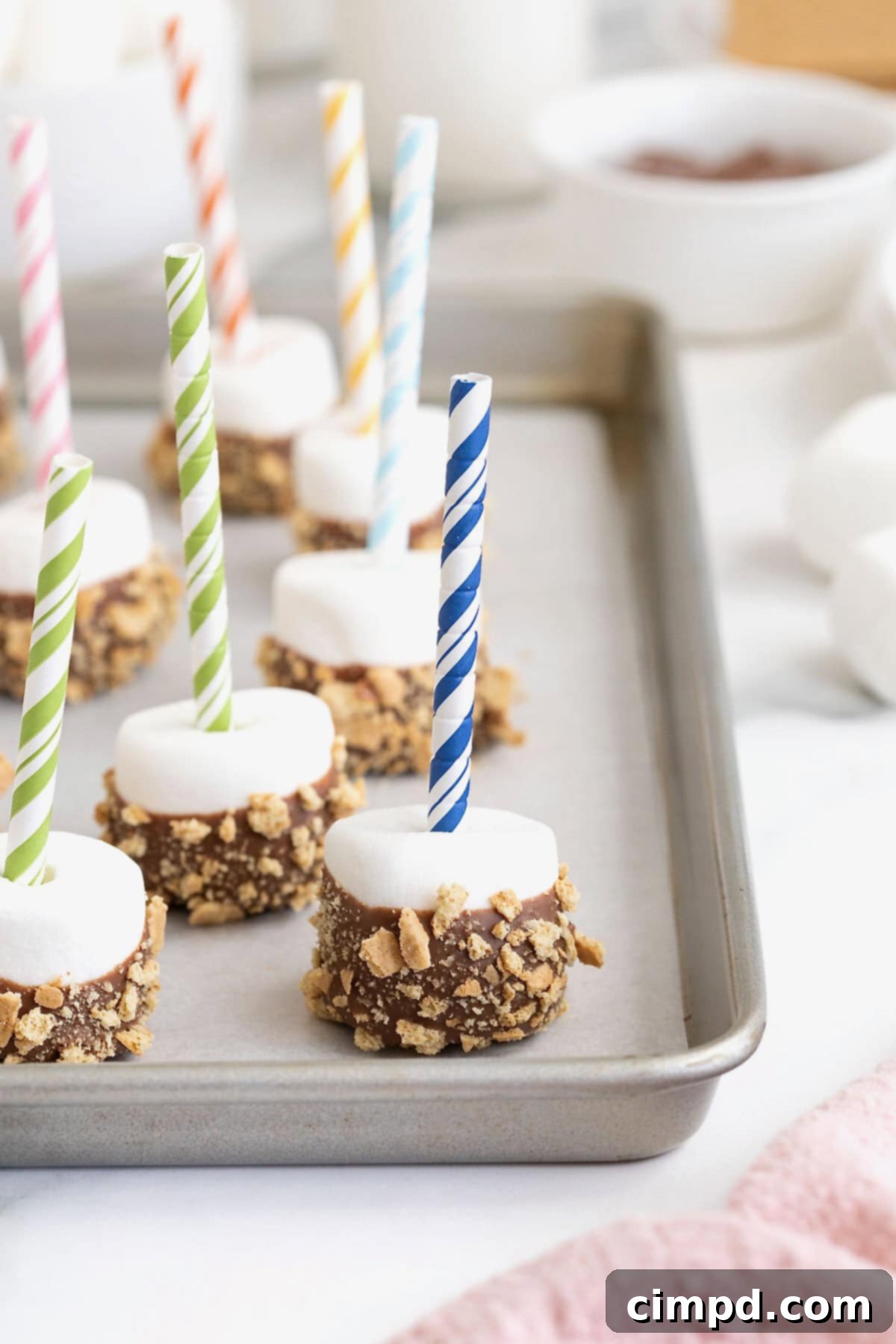 S'mores marshmallow pops on a parchment lined aluminum baking sheet.