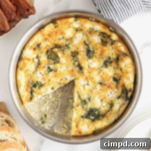 A spinach and goat cheese frittata in stainless steel skillet on a white marble counter.