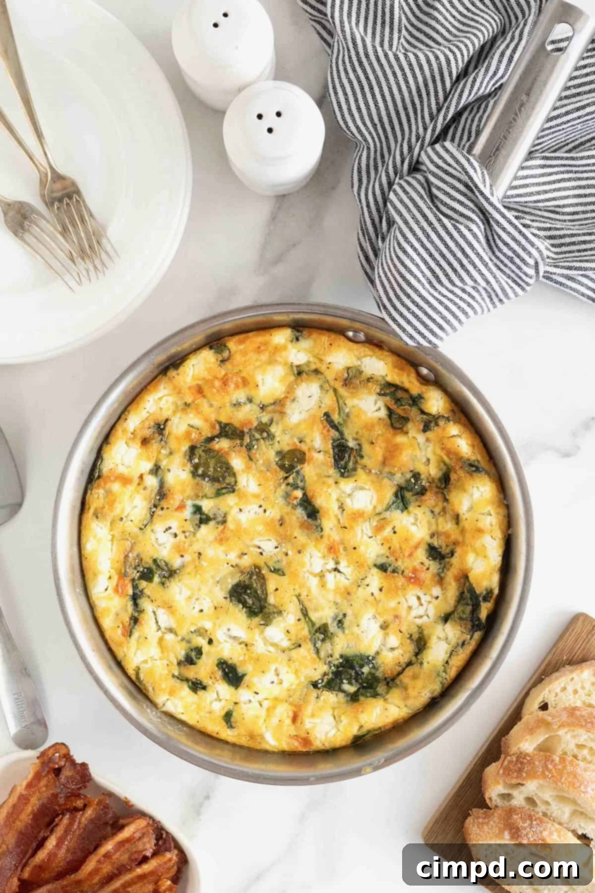 A freshly baked Red Pepper, Spinach, and Goat Cheese Frittata in a gleaming stainless steel pan, sitting on a white marble counter.