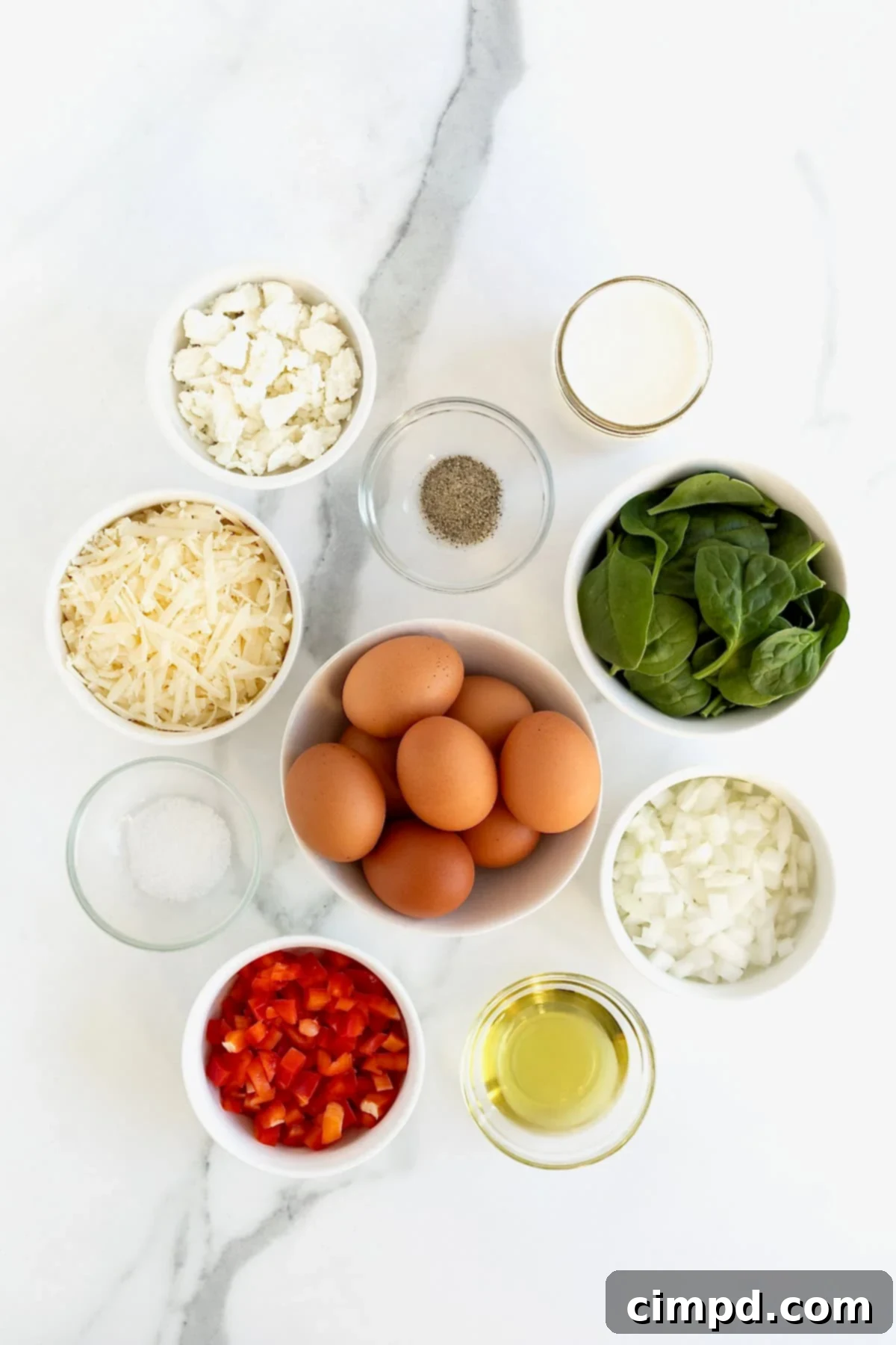 A collection of ingredients for spinach, red pepper, and goat cheese frittata, neatly arranged in small glass dishes on a white marble counter.