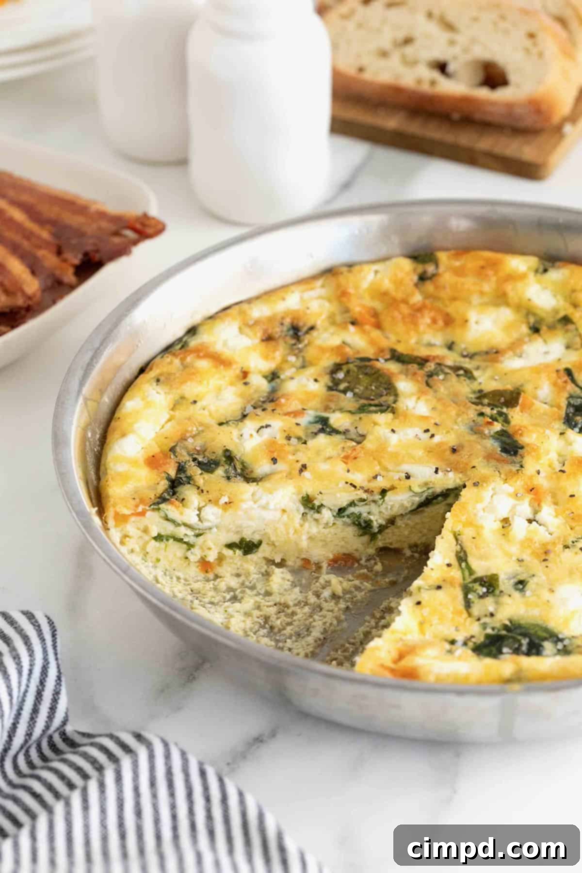 A freshly baked Red Pepper, Spinach, and Goat Cheese Frittata resting in an aluminum pan on a white marble counter, ready for slicing.