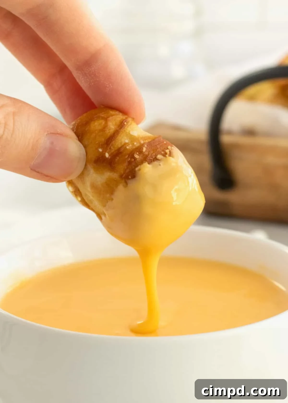 A soft pretzel bite being dipped into a white bowl of cheese sauce, showcasing the creamy texture.