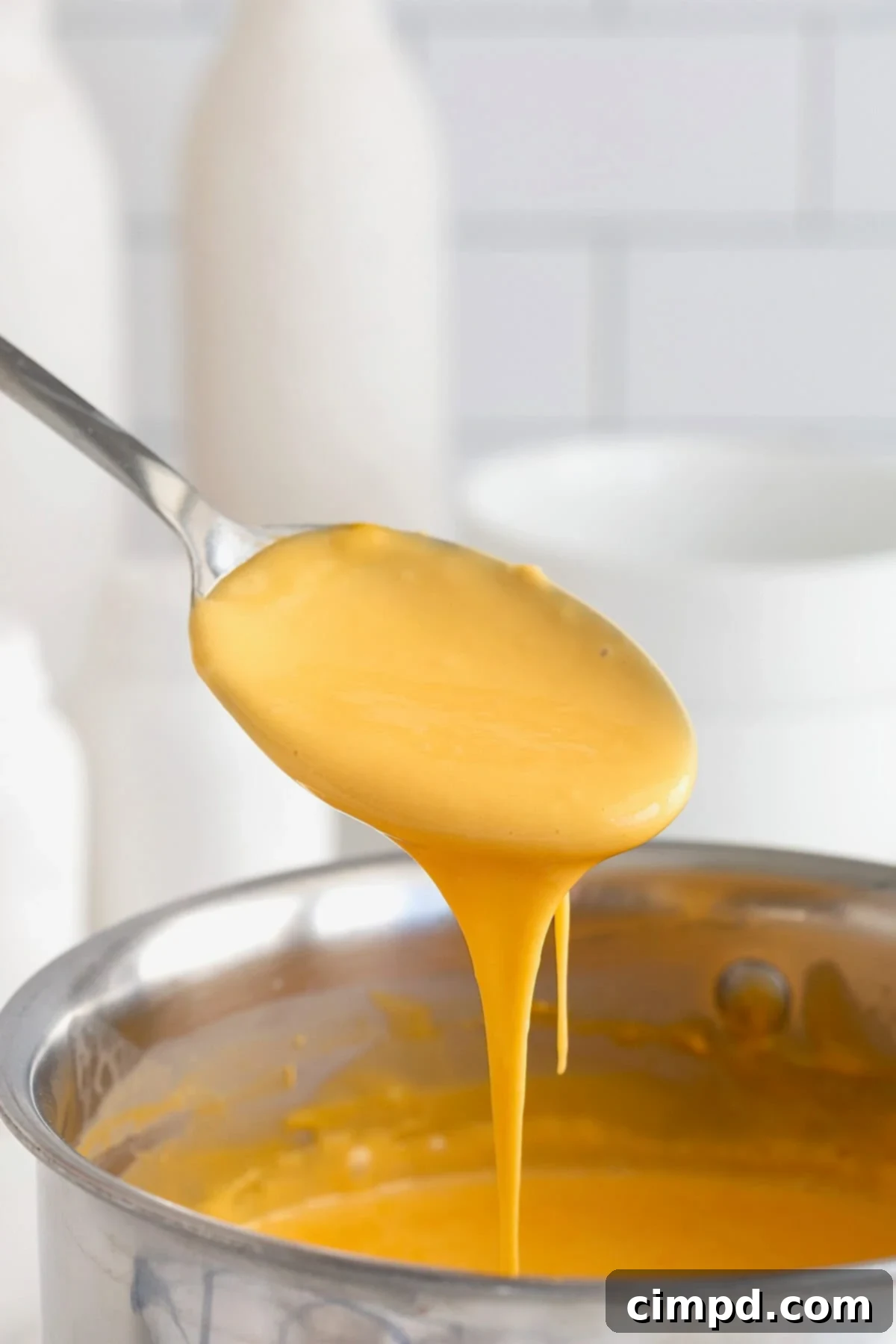 Golden cheese sauce being gracefully poured from a wooden spoon into a gleaming stainless steel pot, ready for storage or reheating.