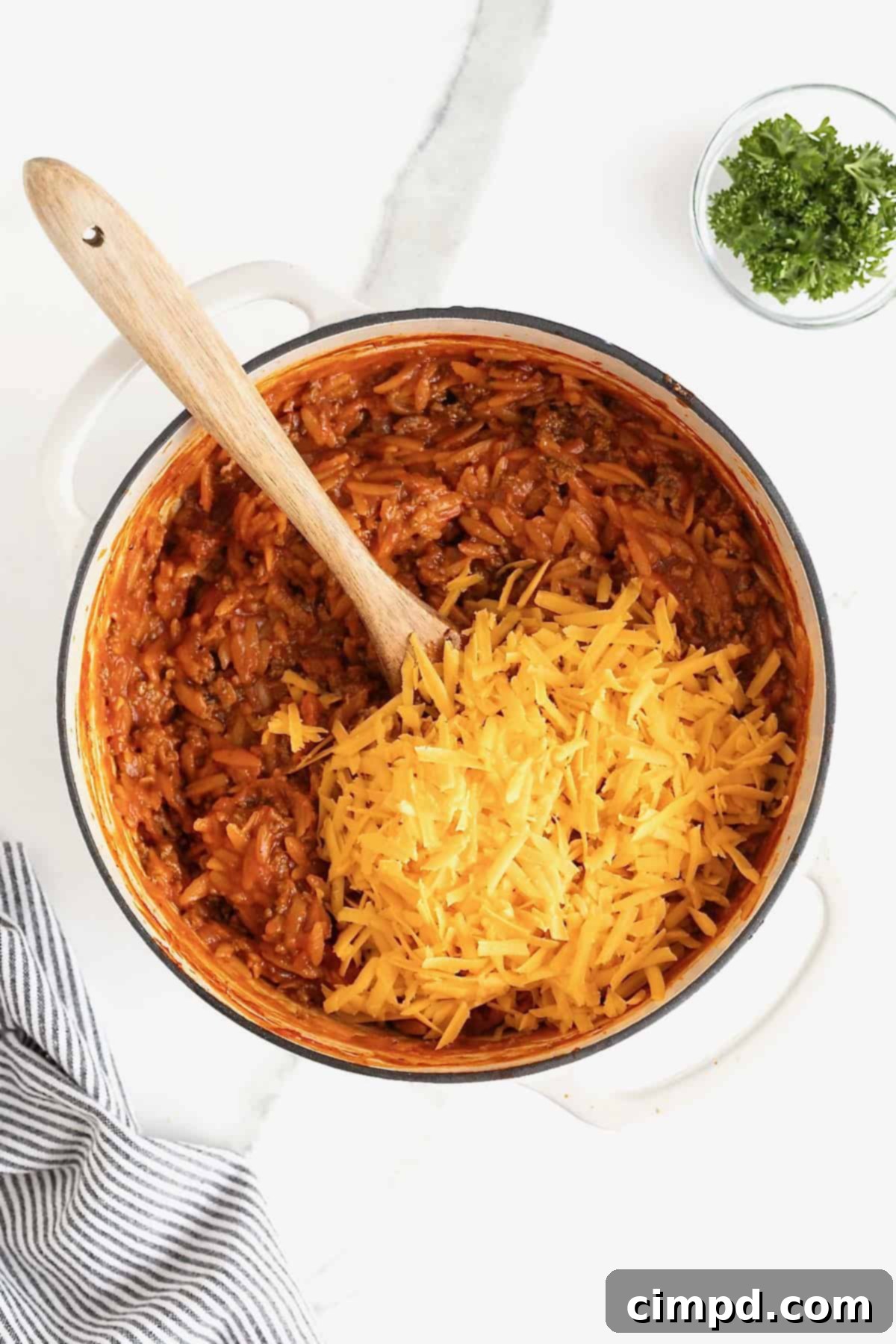 One-Pot Sloppy Joe Orzo 8 Shredded cheddar cheese added to a white dutch oven of sloppy Joe orzo.