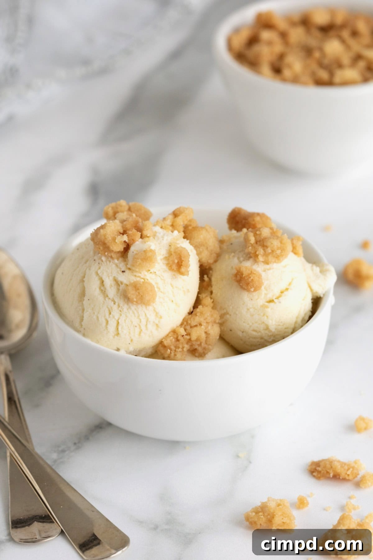 Homemade Streusel Simplified 4 Vanilla ice cream topped with simple streusel in a white bowl next to a metal spoon on a white counter.