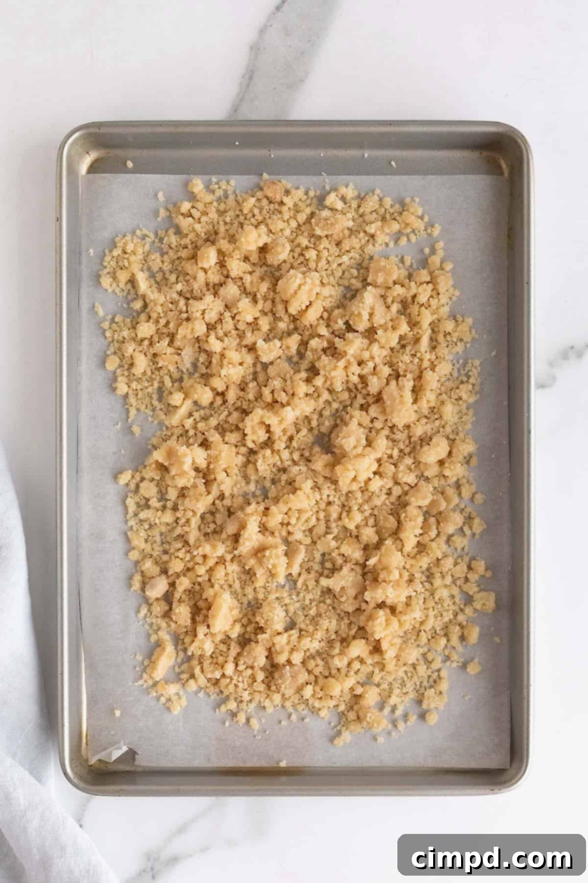 Homemade Streusel Simplified 7 Streusel spread on a parchment lined baking sheet on a white marble counter, ready for baking.