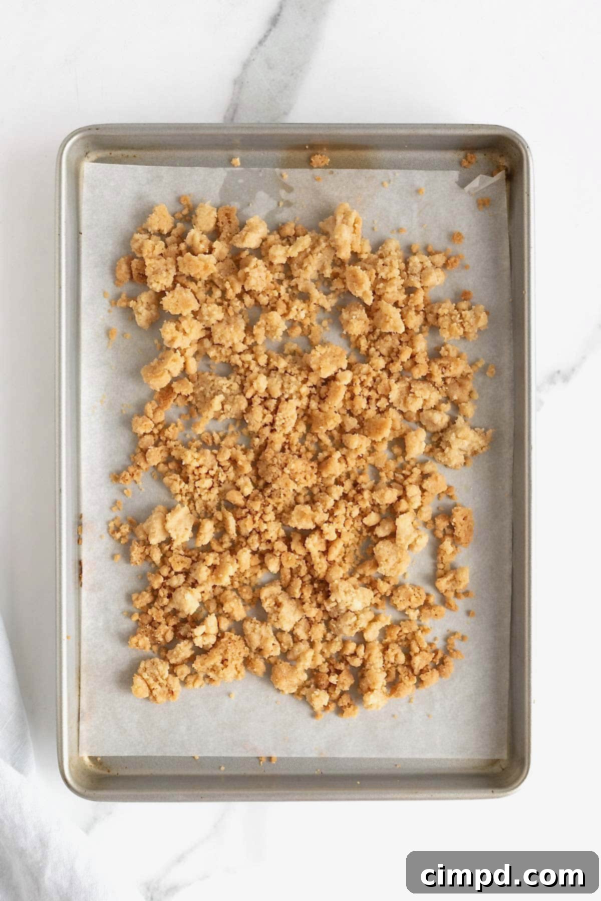 Homemade Streusel Simplified 8 Baked streusel on a parchment lined baking sheet on a white marble counter, golden brown and crisp.
