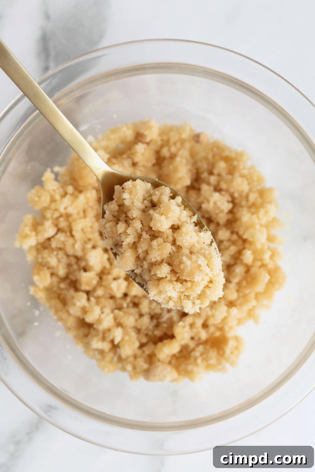 Homemade Streusel Simplified 9 A spoonful of streusel being lifted from a glass bowl, showing its crumbly texture.