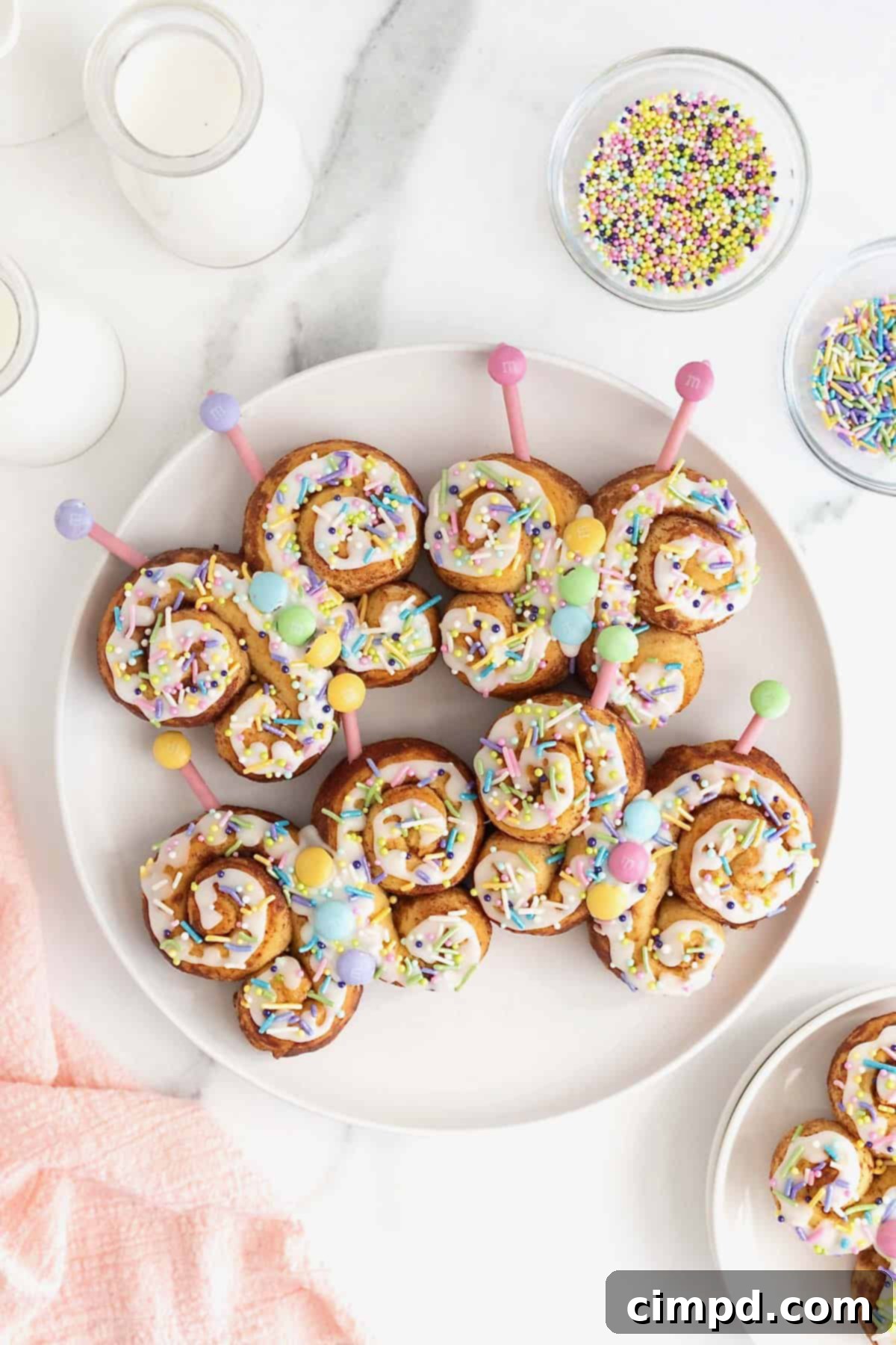 Four butterfly cinnamon rolls decorated with icing and pastel candies on a large white plate.