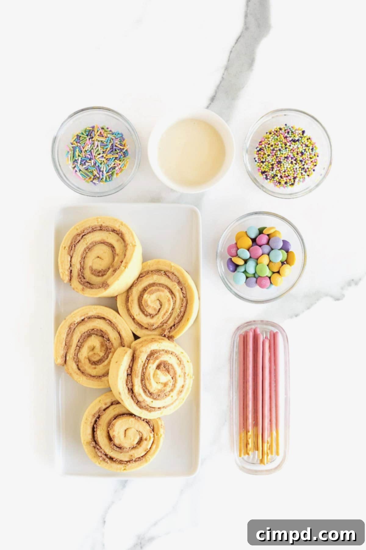 Ingredients to make butterfly shaped cinnamon rolls in small dishes on a white marble counter.