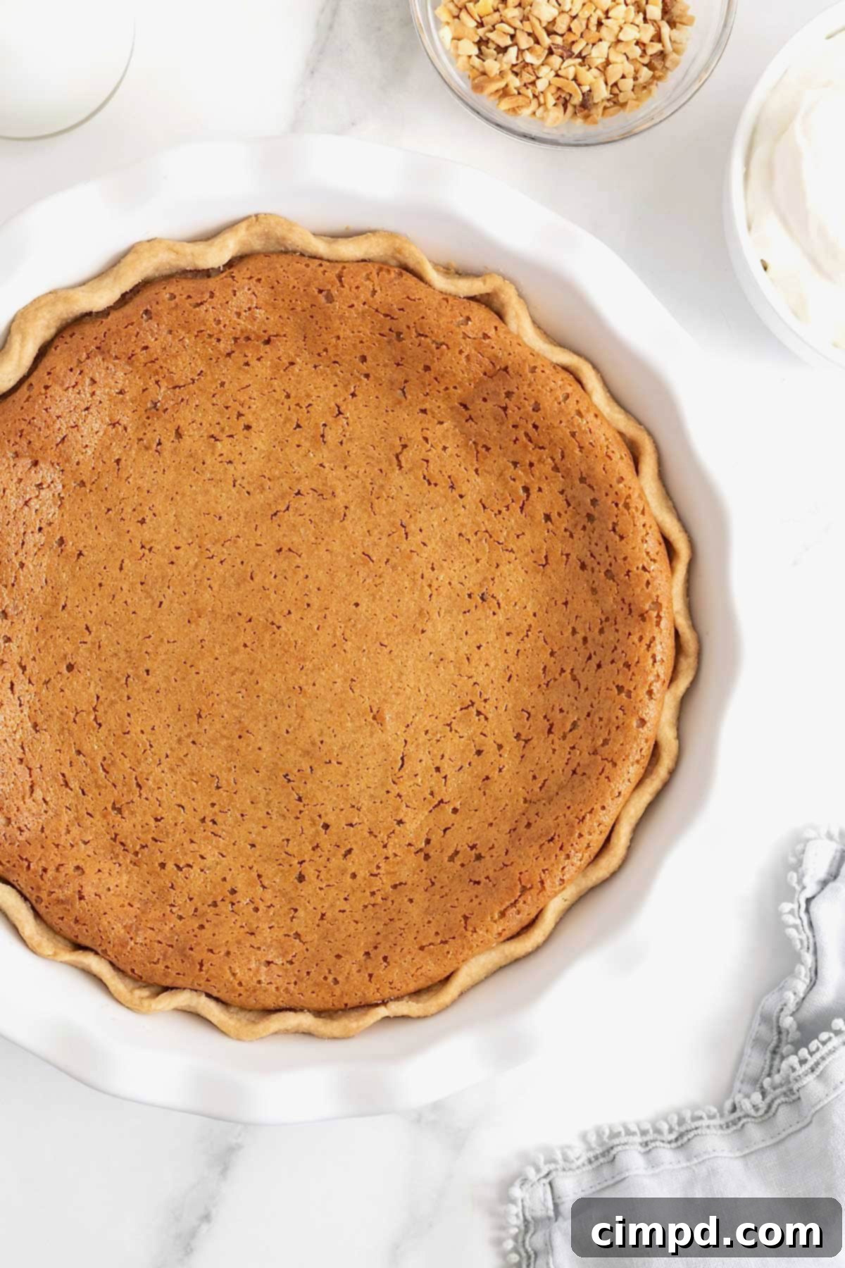 A perfectly baked peanut butter pie with a golden, fluted crust, showcased in a white fluted pie plate, awaiting its moment to be served.