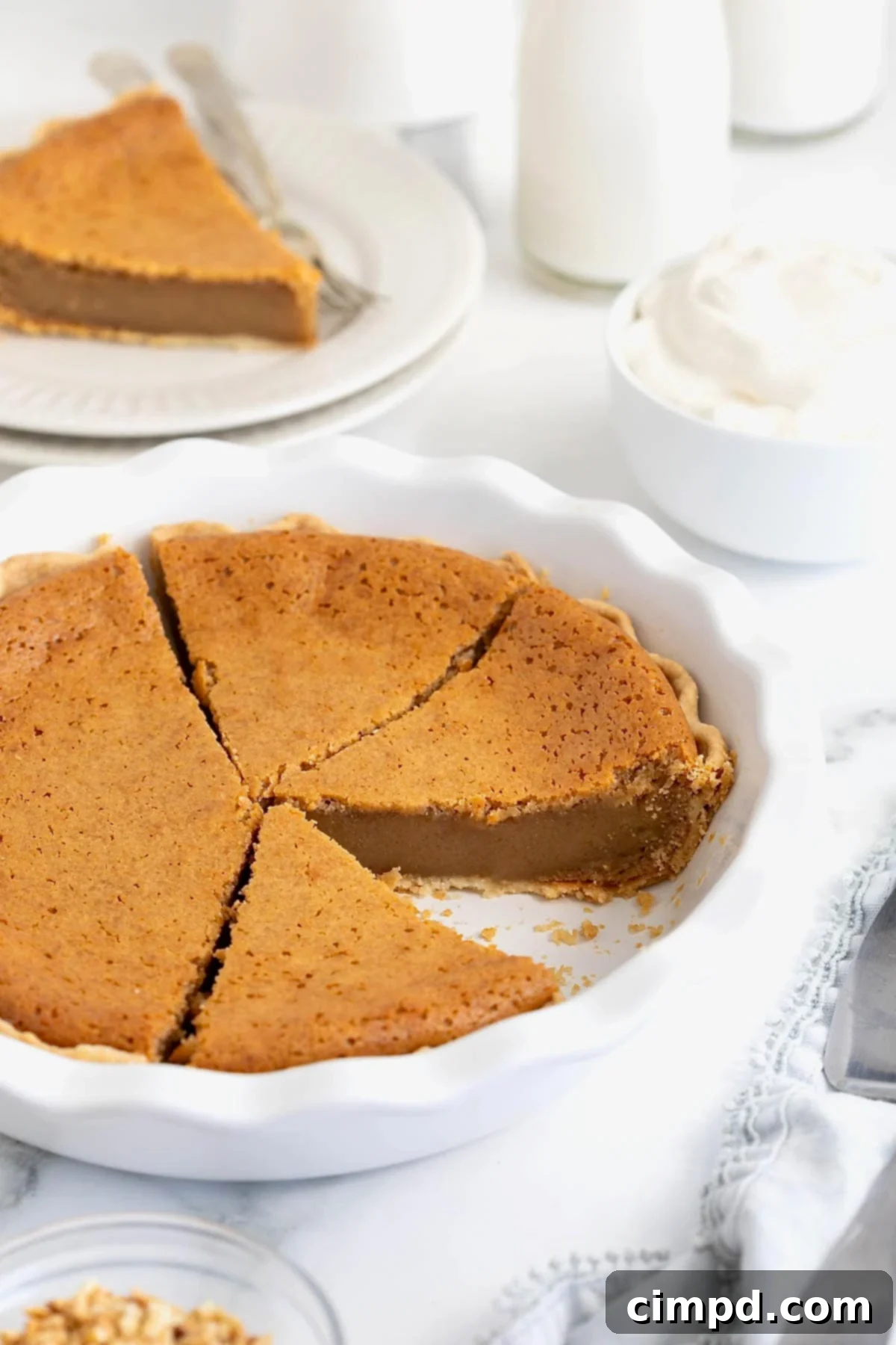 A beautifully baked peanut butter pie featuring a perfectly fluted crust, presented in a white fluted pie plate. A single slice has been removed, revealing the dense, creamy interior.