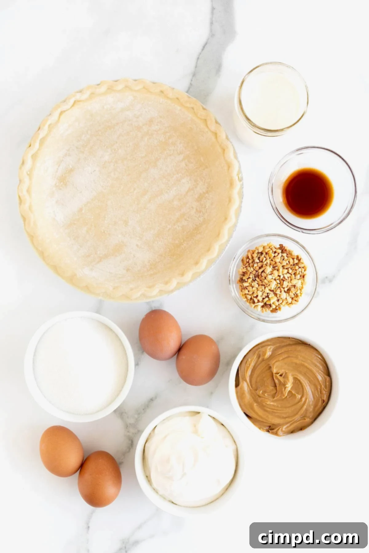 A collection of ingredients for baked peanut butter pie, carefully arranged in small glass dishes on a pristine white marble counter, positioned next to an unbaked pie crust with elegantly fluted edges.
