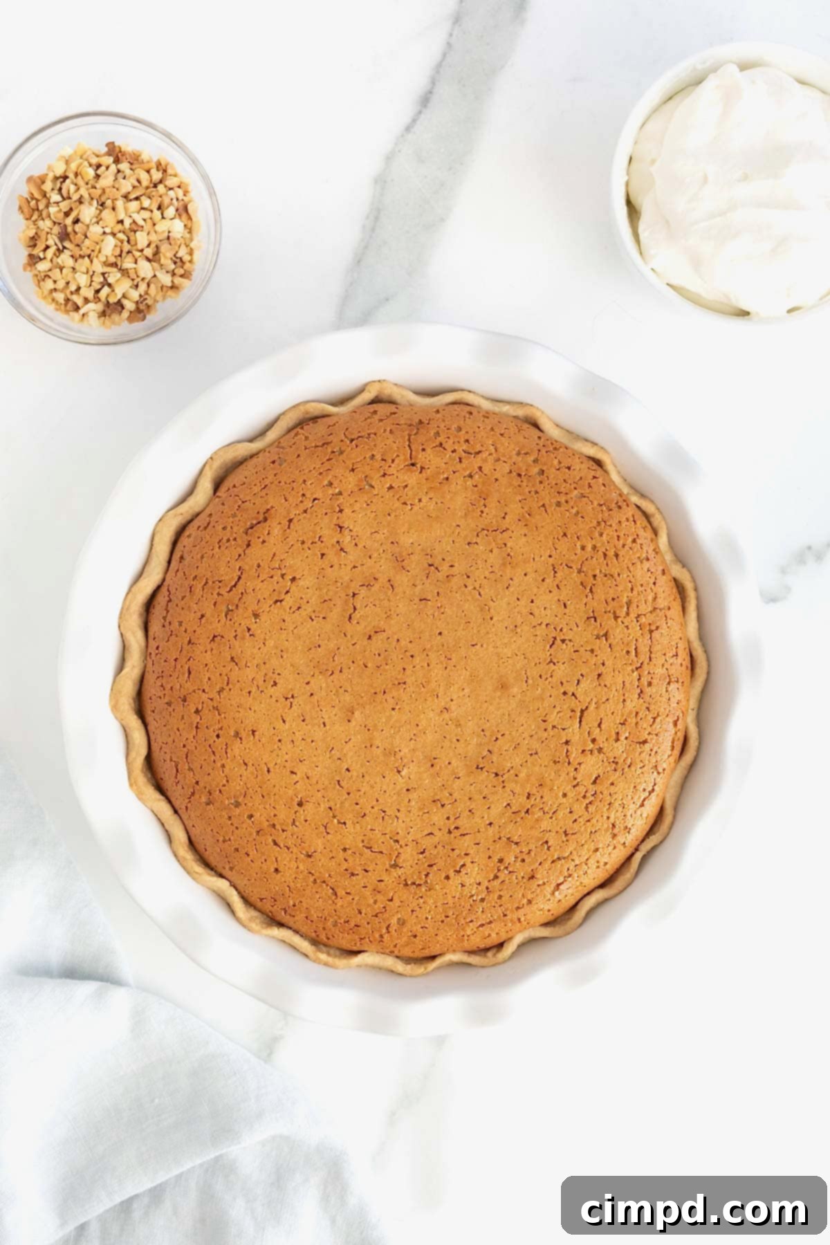 A freshly baked peanut butter pie with a beautifully fluted crust, resting in a white fluted pie plate, cooling after being removed from the oven.