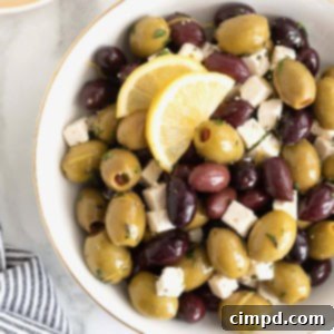 A gold rimmed white serving bowl filled with green and purple olives and small cubes of feta.