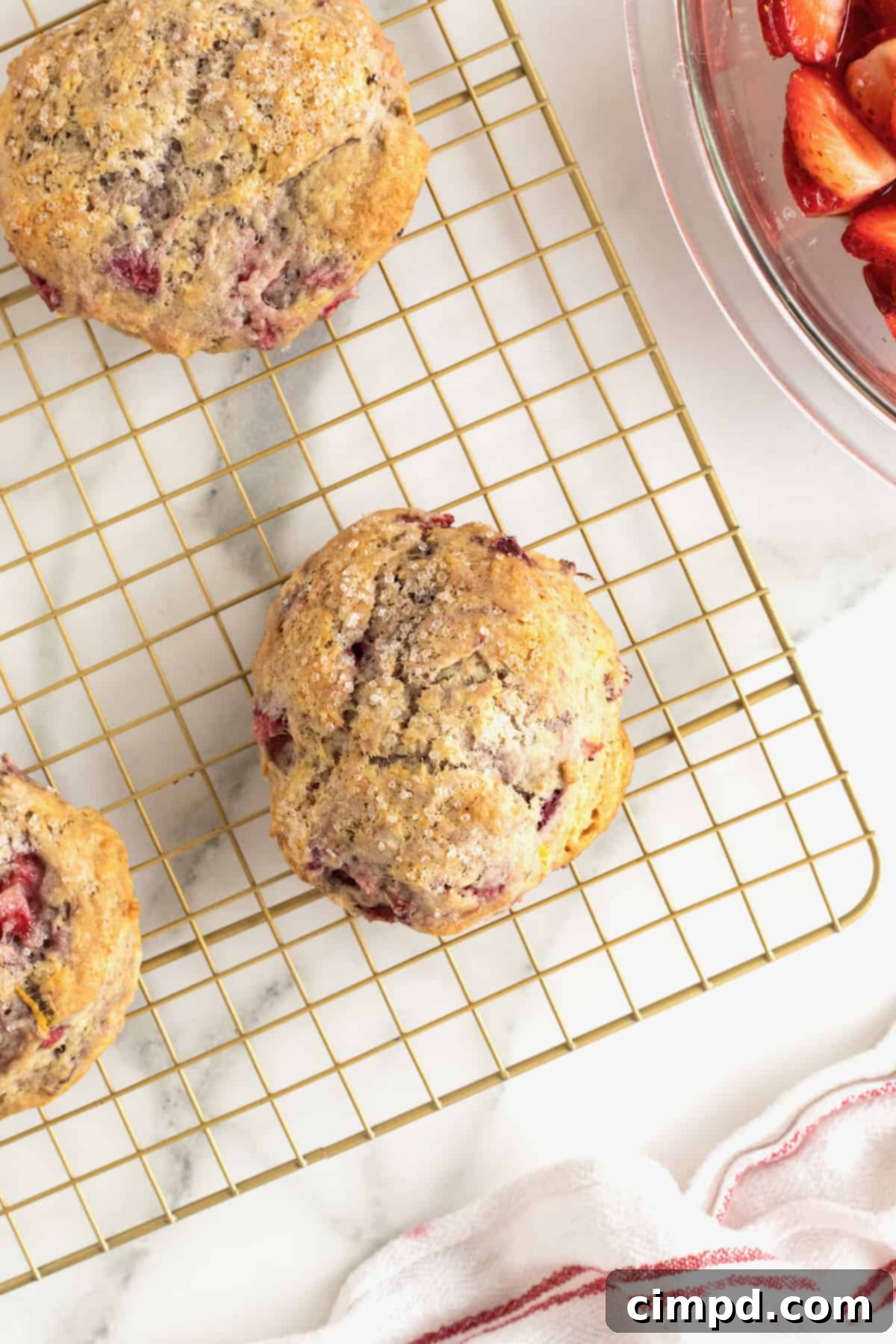 Scone Strawberry Shortcake 10 Three strawberry scones on a gold-toned metal cooling rack on a white marble counter.