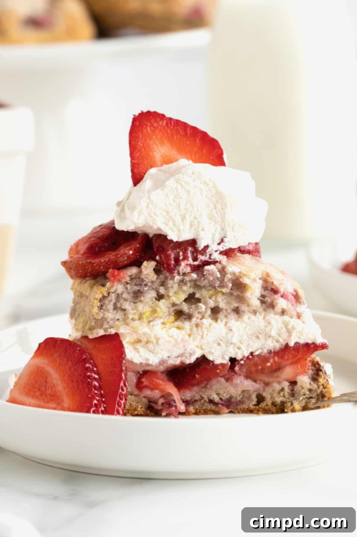 Scone Strawberry Shortcake 3 A double strawberry shortcake made with a strawberry scone on the bottom, a layer of strawberries and whipped cream, another strawberry scone, another layer of strawberries and whipped cream on a round white rimmed plate.