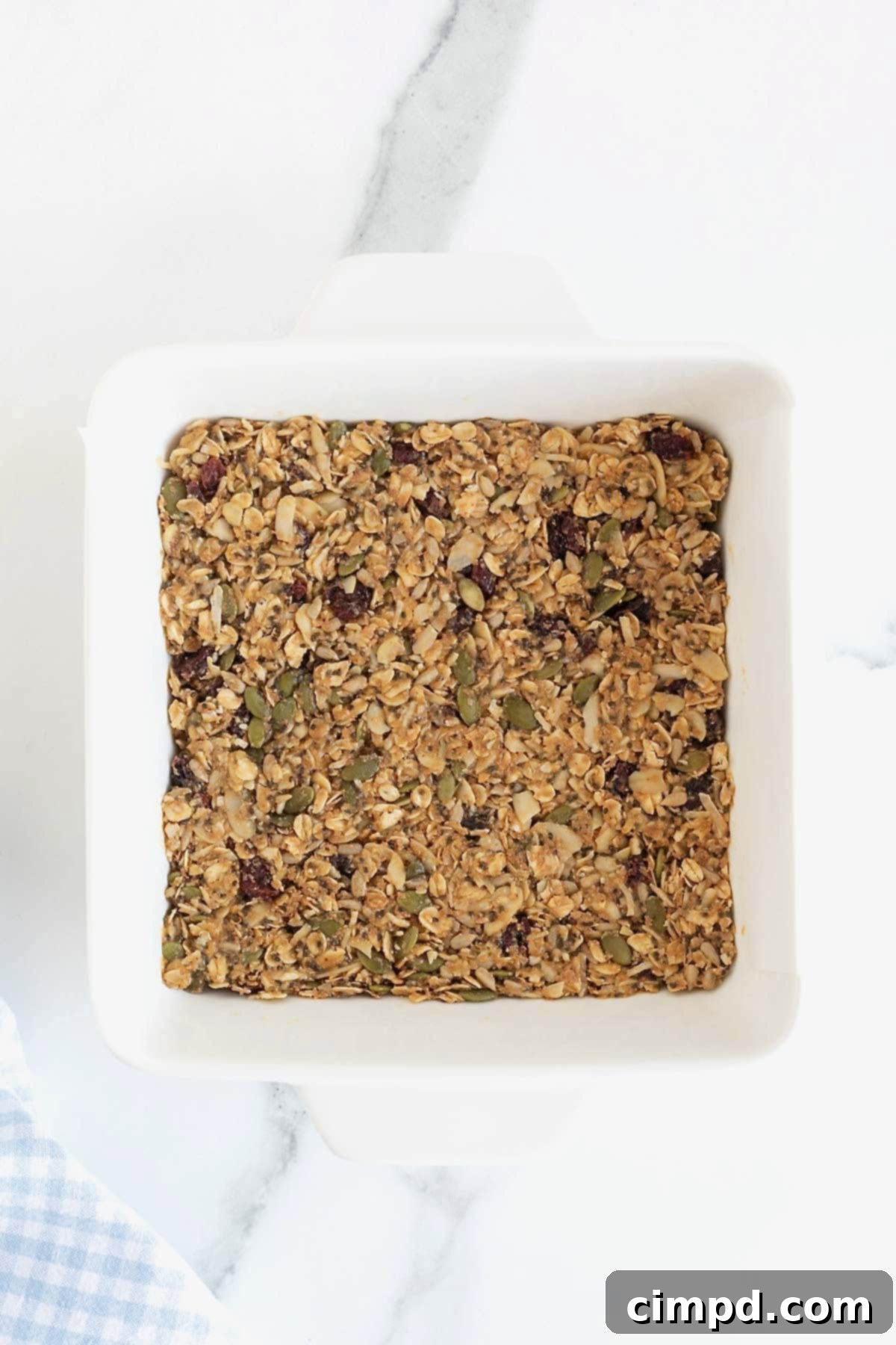 The power bar mixture firmly pressed into a square white baking dish, sitting on a white marble counter, ready for chilling.