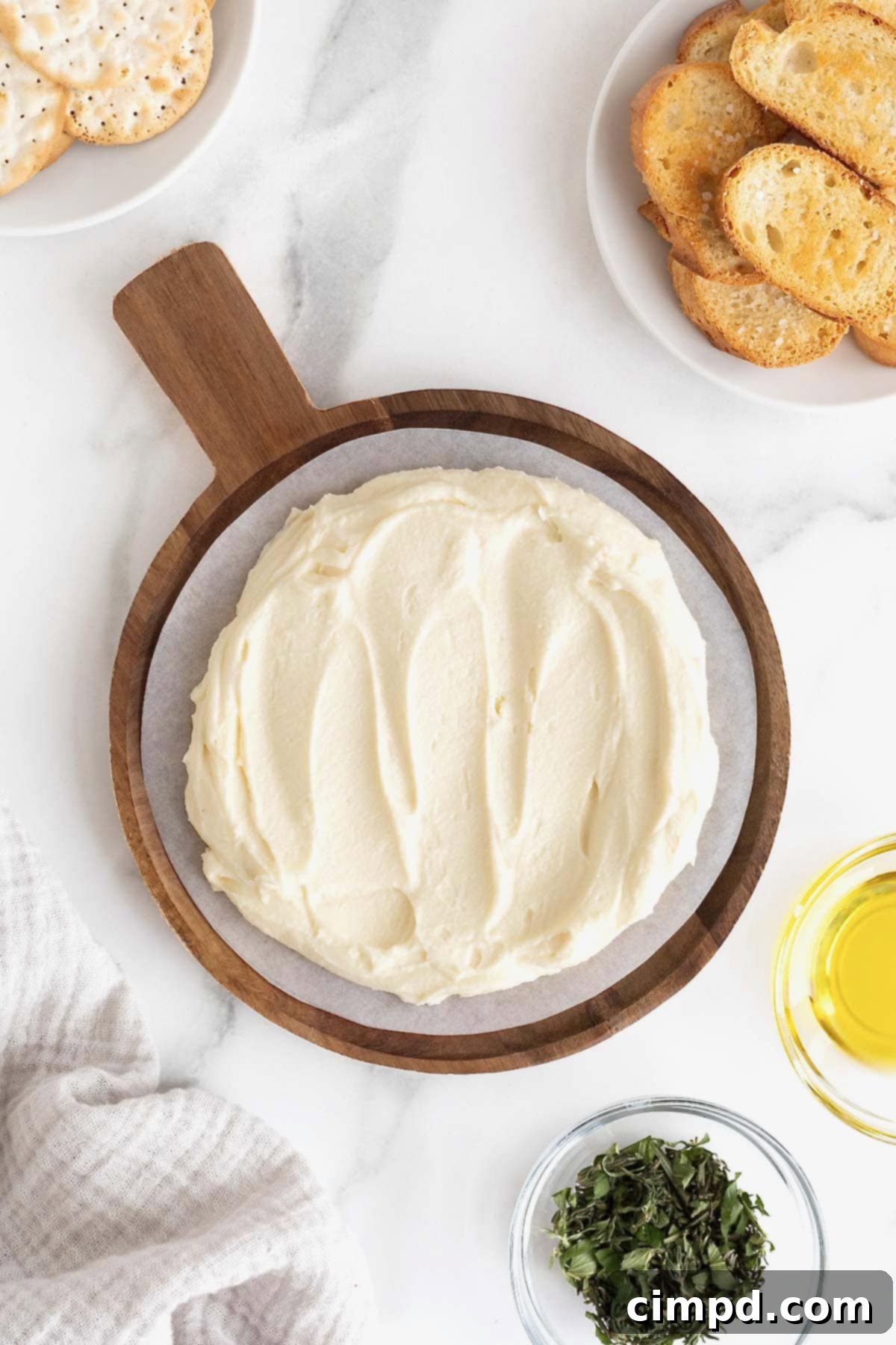 Creamy Whipped Brie 8 Creamy whipped brie elegantly spread across a round wooden serving plate, resting on a pristine white marble counter, ready for the addition of delicious toppings.