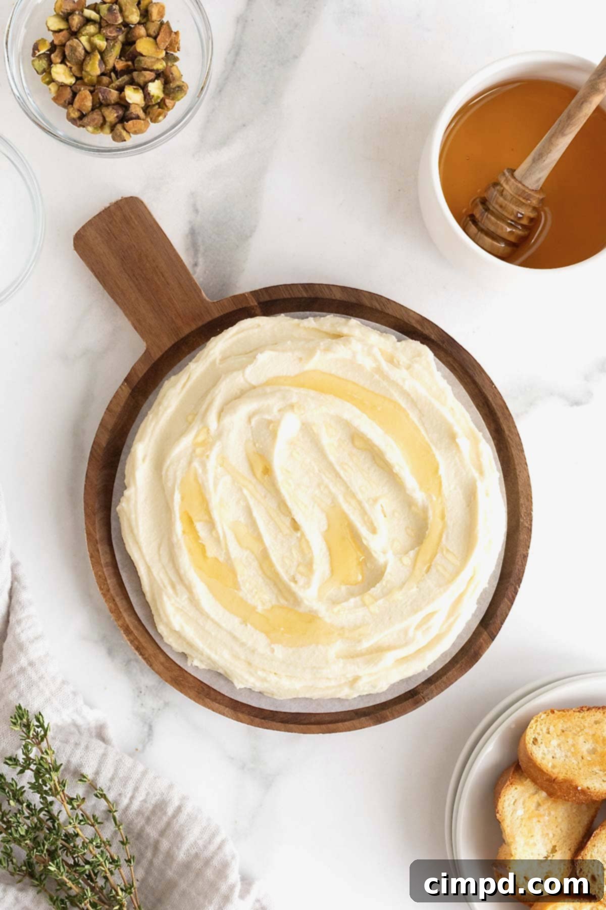 Creamy Whipped Brie 10 A close-up of honey being generously drizzled over a smooth, creamy whipped brie dip, elegantly presented on a wooden serving platter with a handle, preparing it for its sweet garnishes.