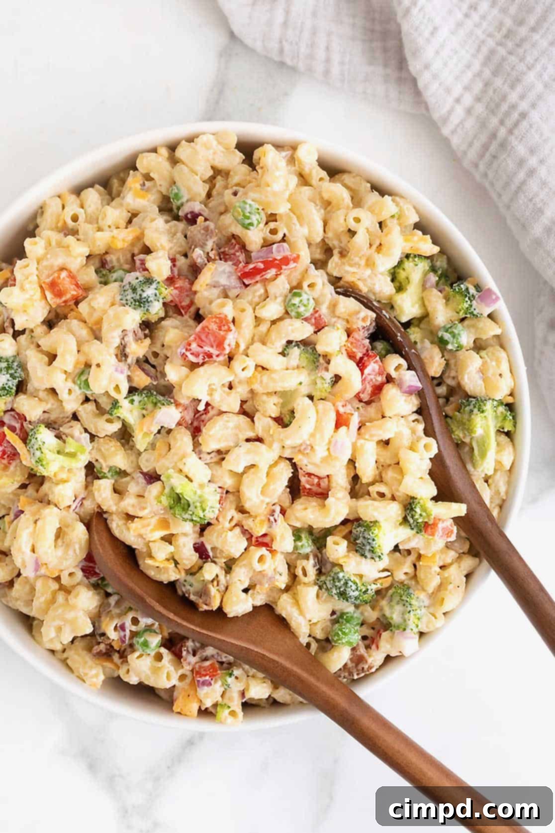 A large white serving bowl of macaroni salad with sweet peas, red onion and cheese, ready to be served.
