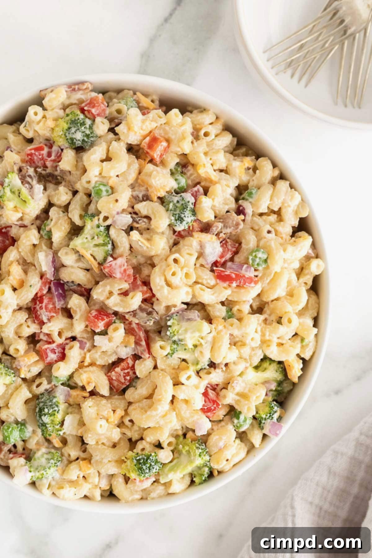 A large white serving bowl of macaroni salad with sweet peas, red onion, and cheese, ready for storage.