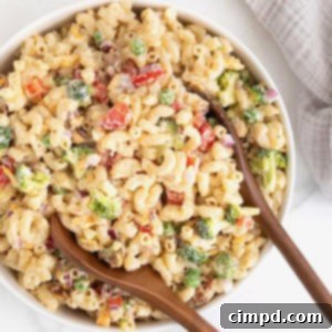A large white serving bowl of macaroni salad with sweet peas, red onion and cheese.