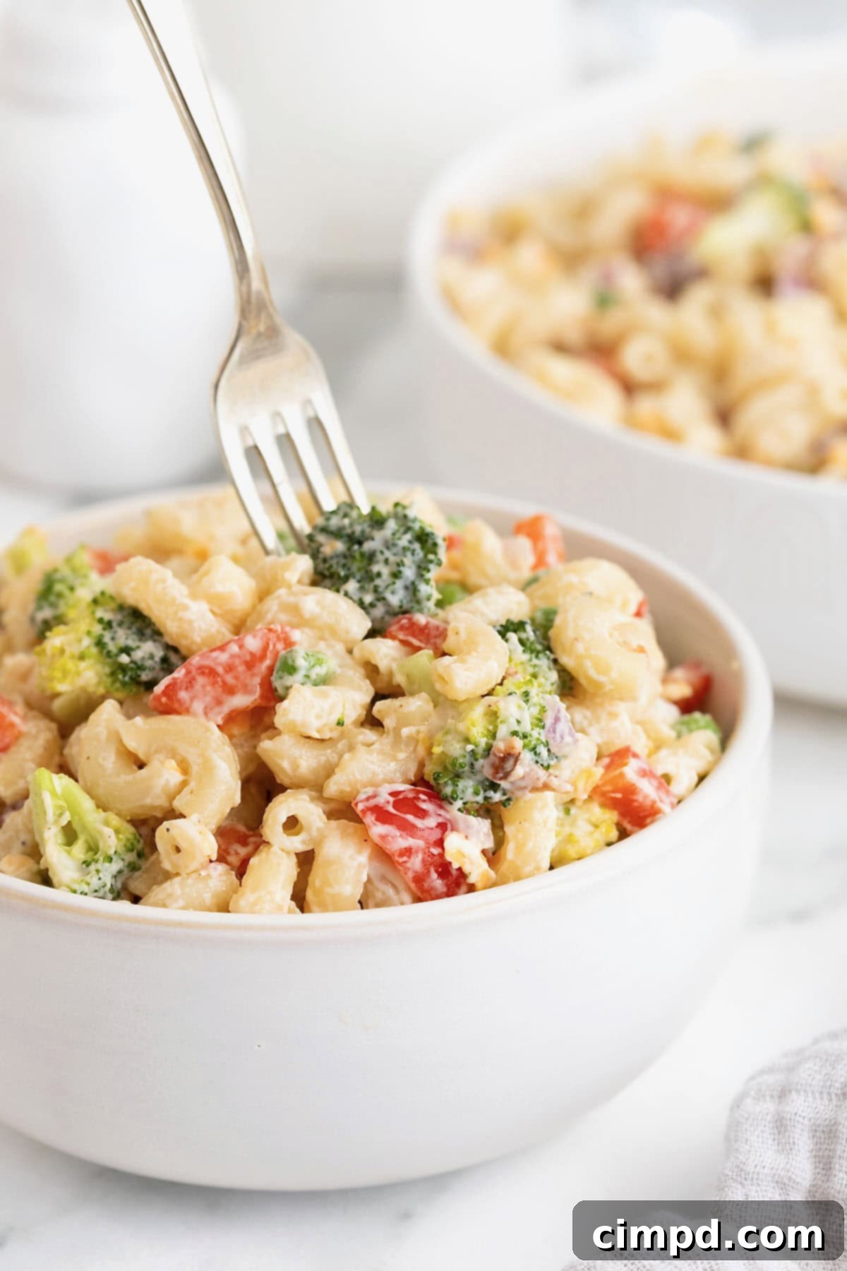 A fork in spearing a small piece of broccoli in a bowl of creamy pasta salad, showcasing the texture.
