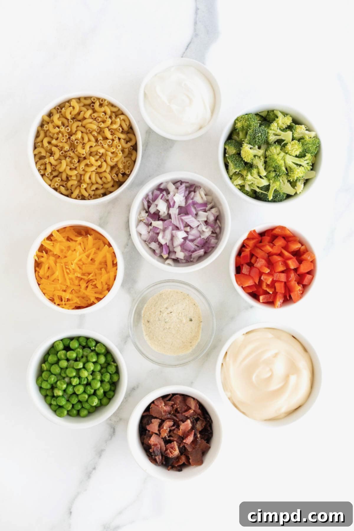 Ingredients for bacon ranch macaroni salad neatly arranged in small white dishes on a white marble counter, ready for preparation.