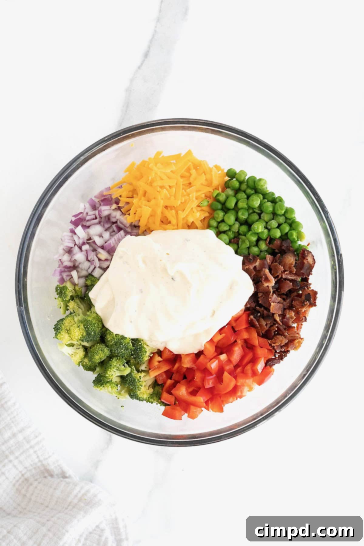 Creamy ranch dressing being poured over the mixed ingredients of pasta salad in a large bowl.