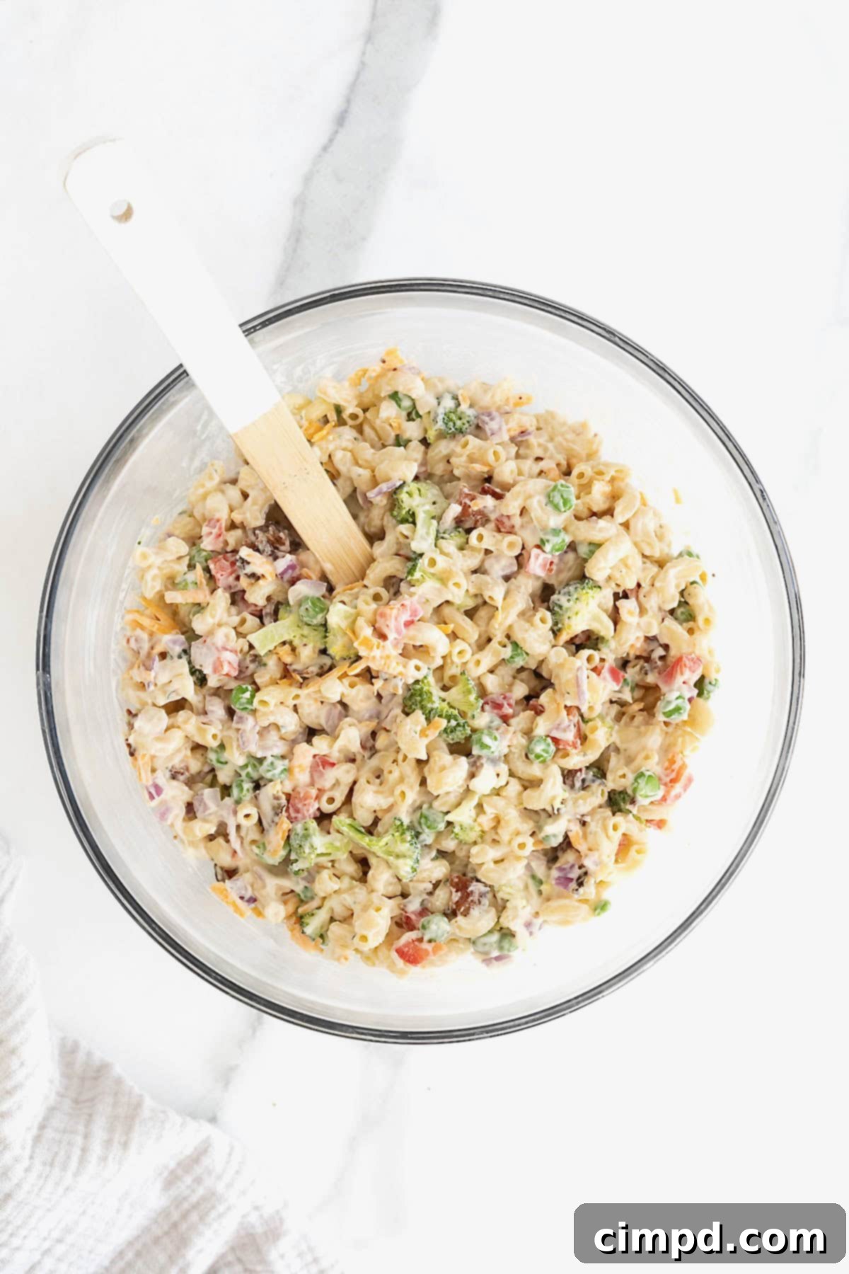 Bacon ranch macaroni salad in a large glass mixing bowl with a white handled wooden spoon sticking out, perfectly mixed.