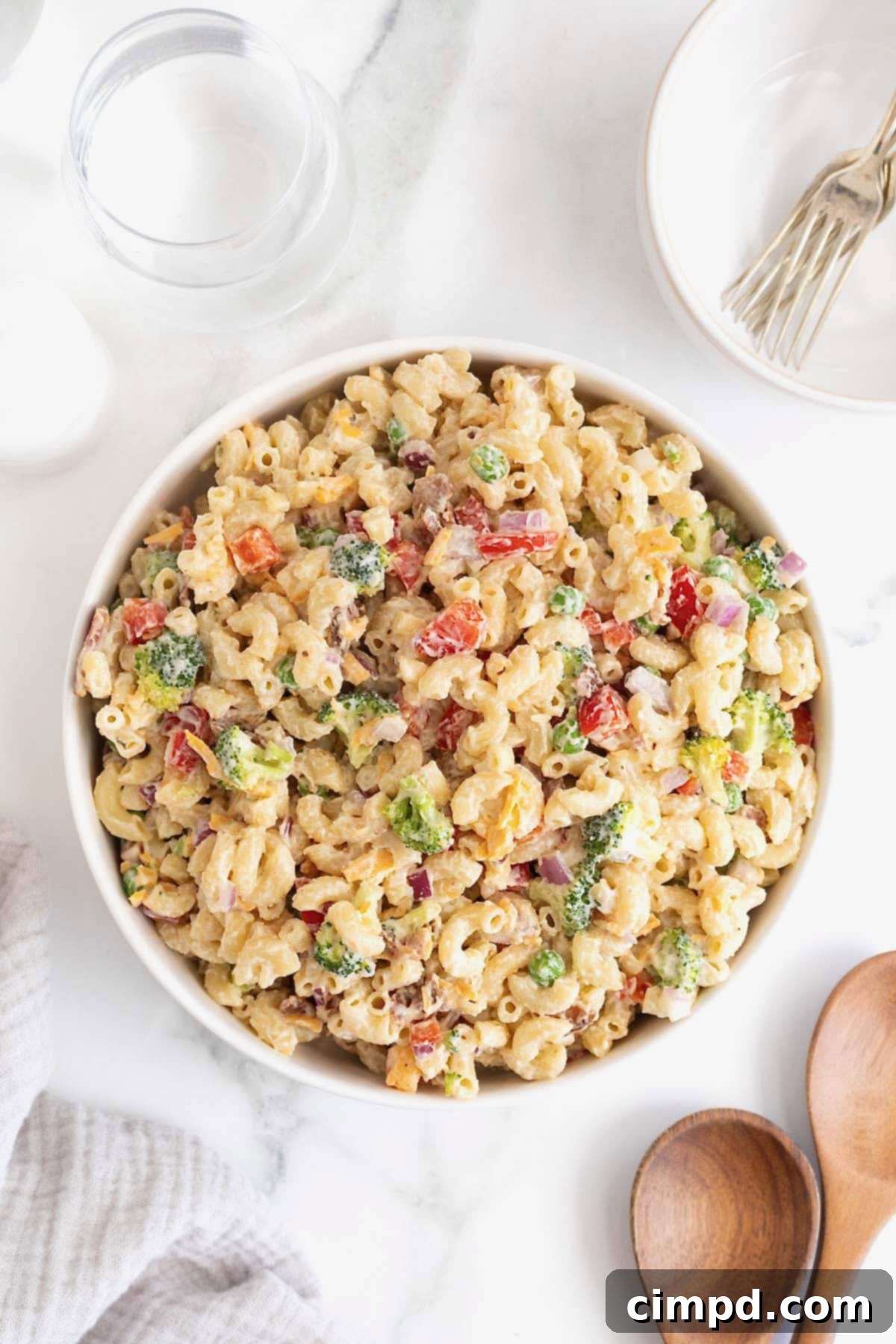 A large white serving bowl of macaroni salad on a white marble counter, perfectly chilled and ready to serve.
