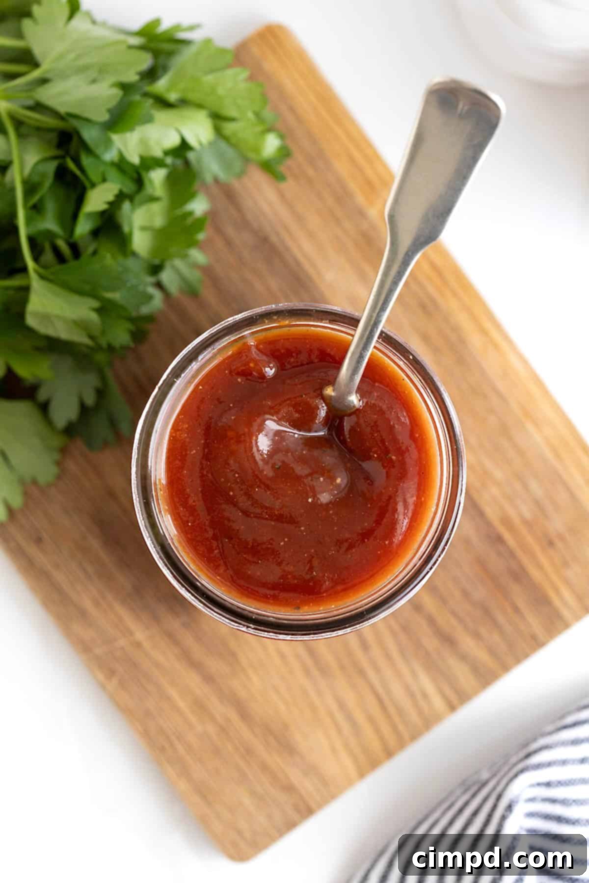 Handcrafted Barbecue Sauce 3 A clear glass jar brimming with rich, homemade barbecue sauce, featuring a spoon elegantly submerged within, ready for tasting.