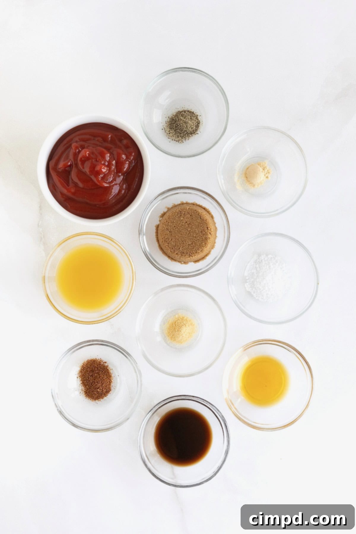Handcrafted Barbecue Sauce 5 A vibrant collection of small glass dishes showcasing the fresh ingredients for homemade barbecue sauce: ketchup, brown sugar, orange juice, Worcestershire, liquid smoke, and various spices arranged neatly on a white marble countertop.