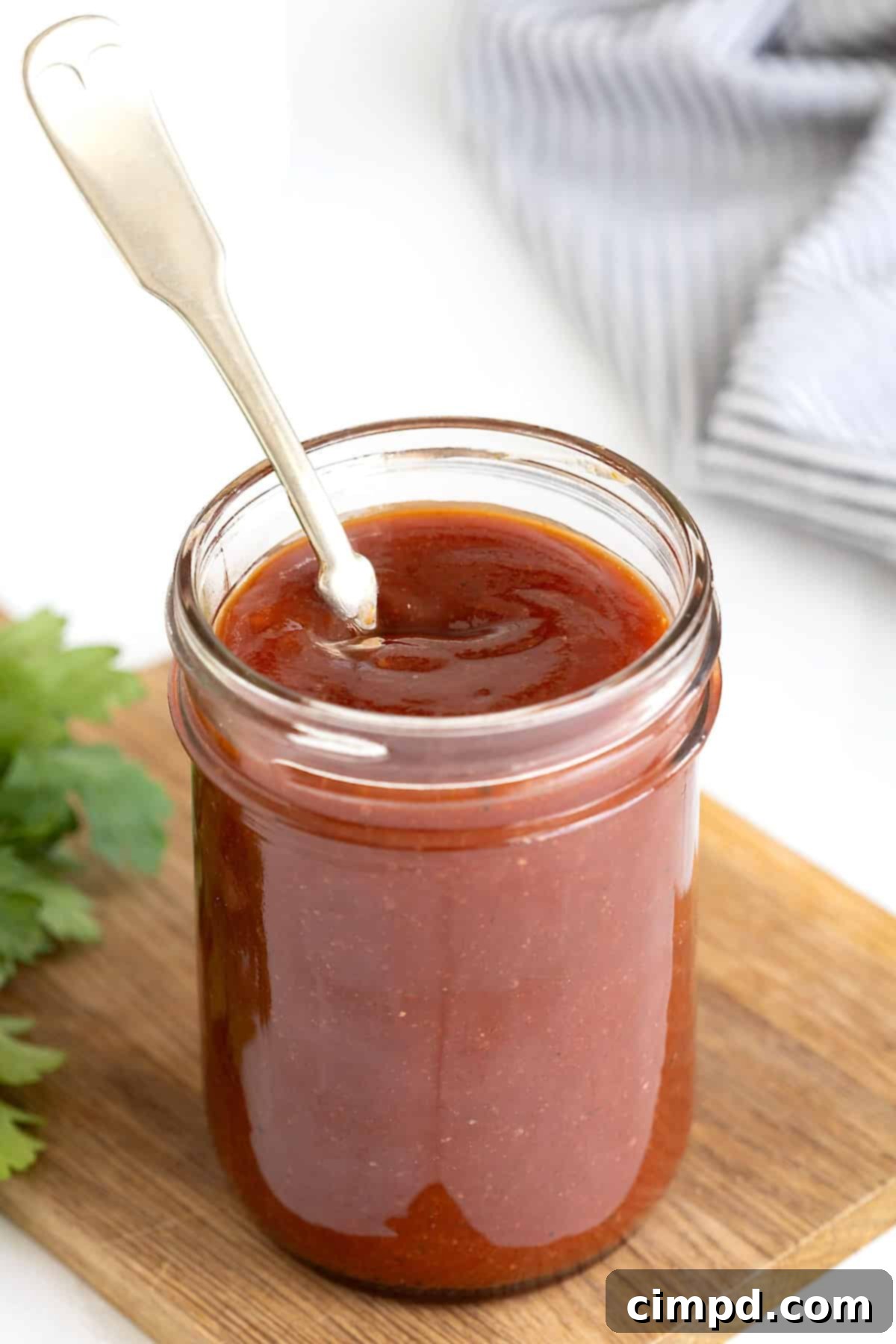 Handcrafted Barbecue Sauce 7 A wide-mouth glass jar filled with luscious, homemade barbecue sauce, with a spoon standing upright, perfectly showcased against a warm, inviting backdrop.