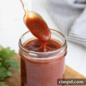 Handcrafted Barbecue Sauce 9 A spoon being dipped into a wide mouth mason jar of barbecue sauce on a wooden cutting board.