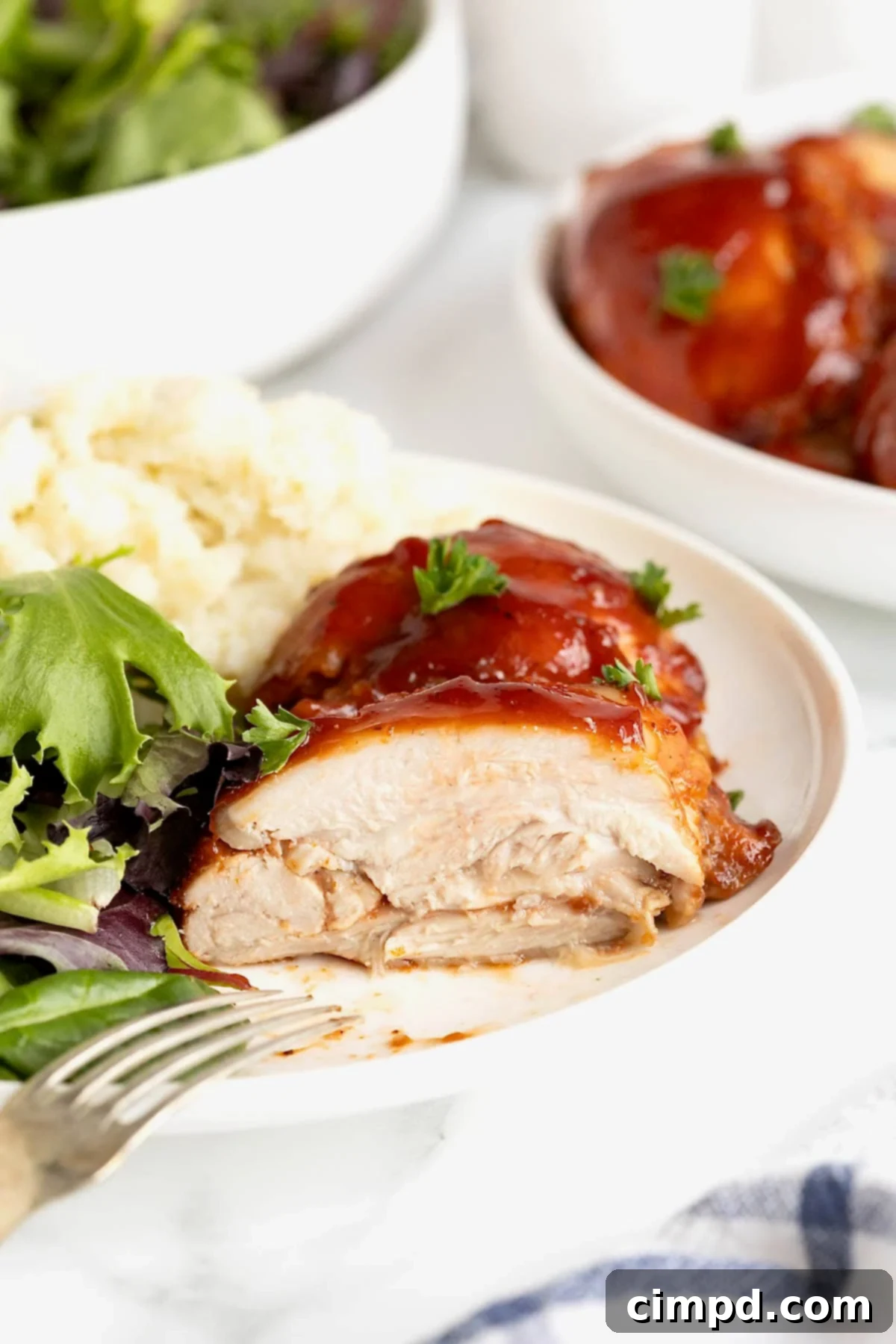 A piece of barbecue chicken on a white dinner plate next to mashed potatoes and a green salad.